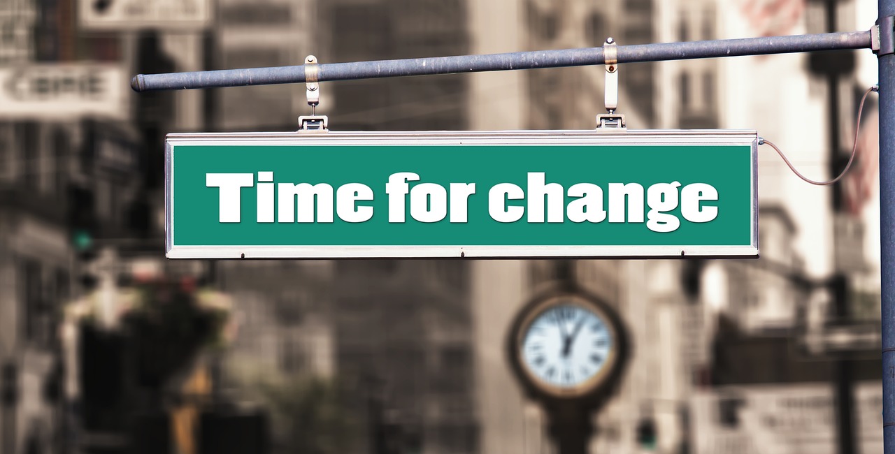 Street sign hanging from a metal bar with the phrase "Time for change" written in bold, white letters on a green background.